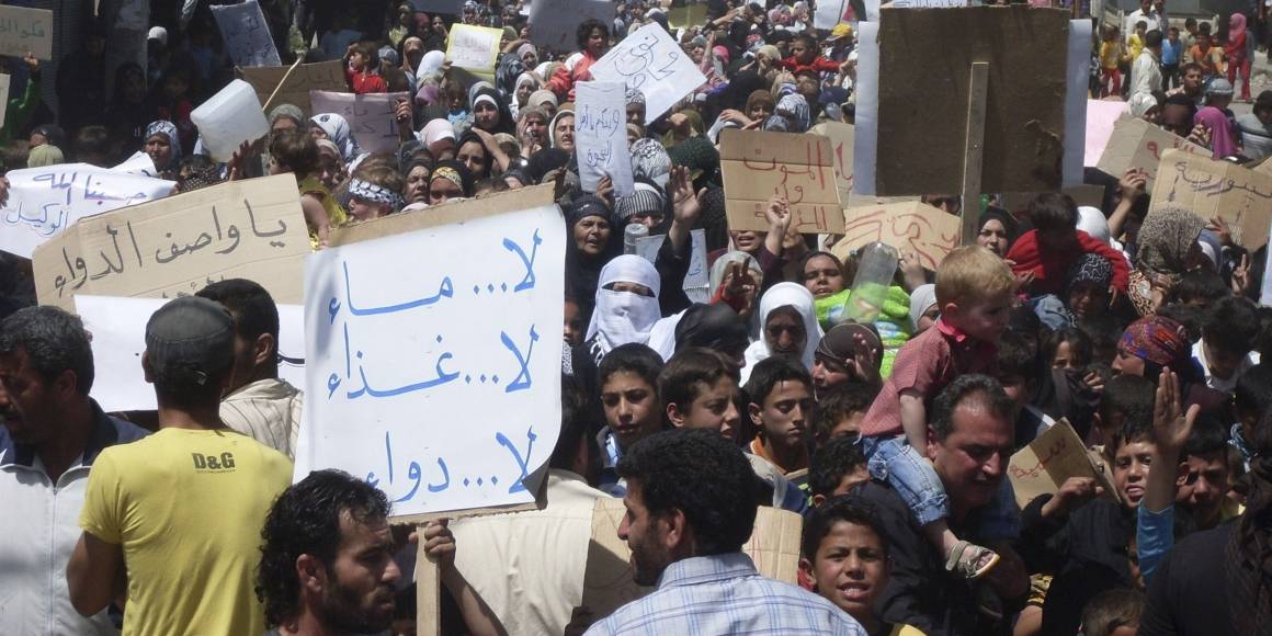 Folk samler seg i byen Nawa, nær Deraa i april 2011, i en av de første demonstrasjonene mot regimet. På skiltet står det "Ikke noe vann, ikke noe medisin, ikke noe mat." Foto: REUTERS/Handout